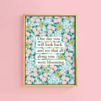 A framed print with a floral pattern and a quote about blooming.