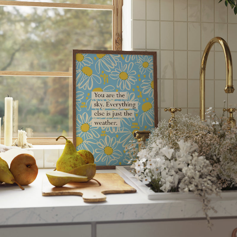 Decorative kitchen scene with a framed quote, fruits, and flowers.