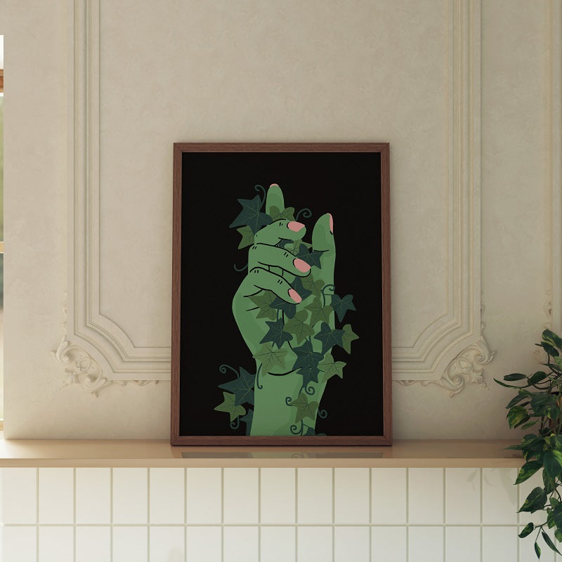 Framed artwork of a green hand with leaves on a black background, displayed on a shelf.