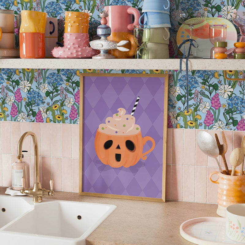 Kitchen counter with colorful mugs, a framed picture of a pumpkin mug, and floral wallpaper.