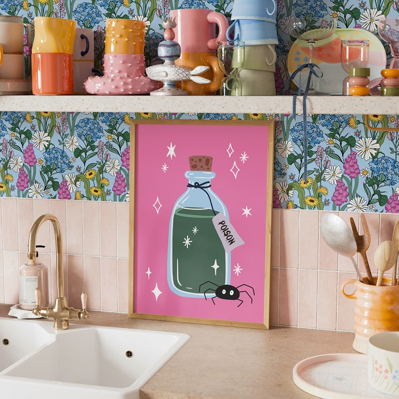 Kitchen counter with colorful mugs, a framed picture of a potion bottle, and floral wallpaper.