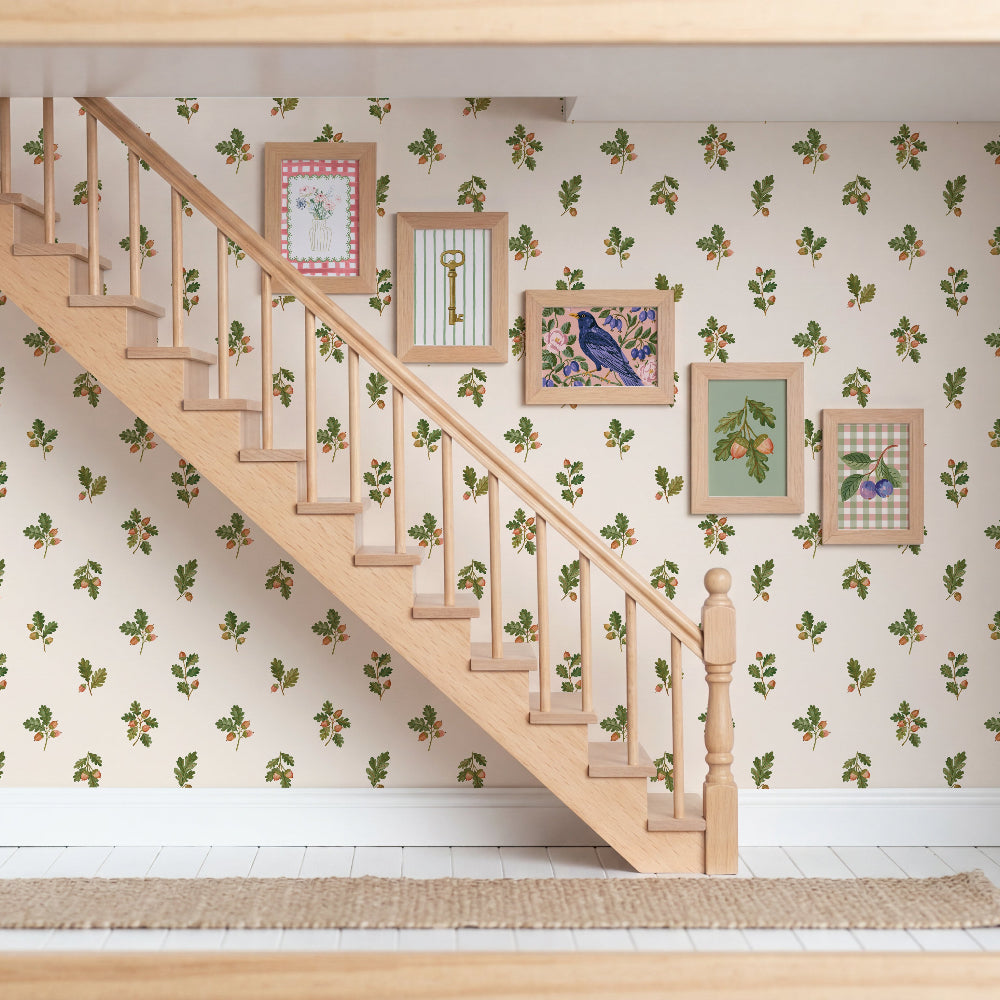 A miniature dollhouse interior featuring a wooden staircase, wallpaper with a green and brown leaf pattern, and several small framed pictures on the wall.