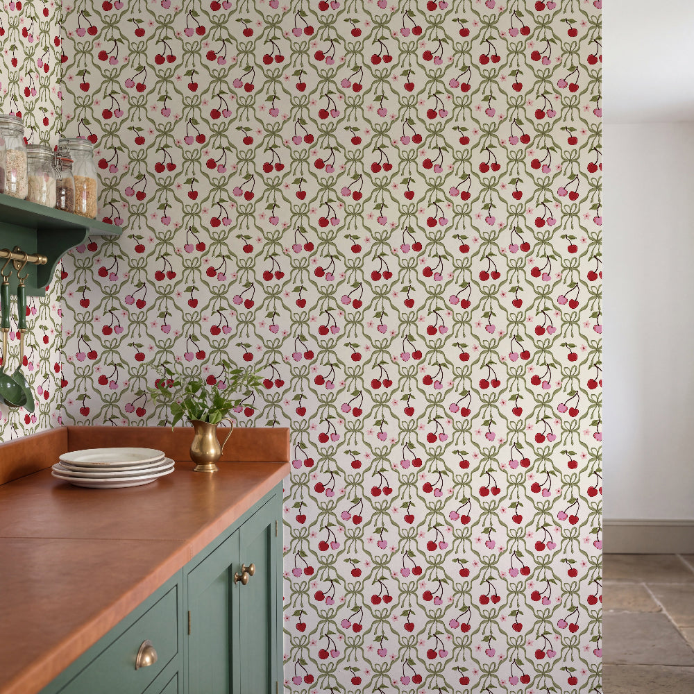 A kitchen interior featuring a cream wallpaper with a repeating red cherry and green vine pattern, paired with a copper-look countertop and teal cabinets.