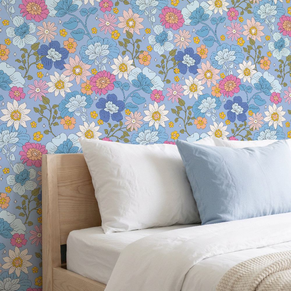 Florarium wallpaper in Powder Blue with delicate whimsical florals in soft pinks, blues and yellows on a muted blue background, styled in a bedroom