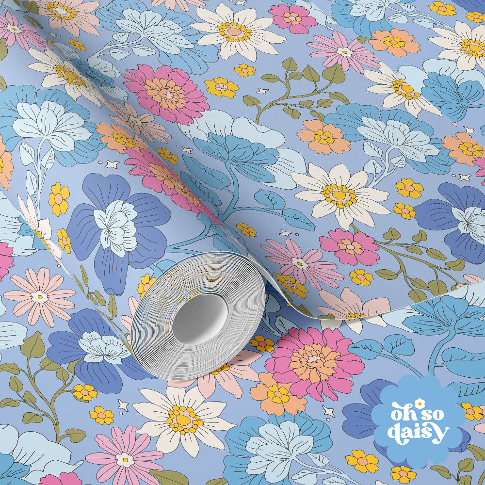 Florarium wallpaper in Powder Blue with delicate whimsical florals in soft pinks, blues and yellows on a muted blue background, styled in a bedroom