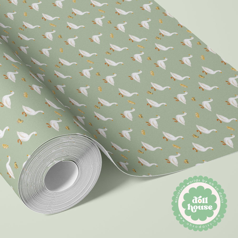 A roll of wrapping paper with a sage green background, featuring a repeating pattern of white ducks and gold ducklings, shown partially unrolled. A circular logo for 'dôi house' is visible in the bottom right corner.