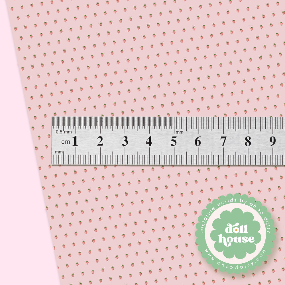A close-up of a light pink perforated fabric or mesh material with a metal ruler laid across it to show scale, plus a green circular logo reading “doll house” in the lower right.