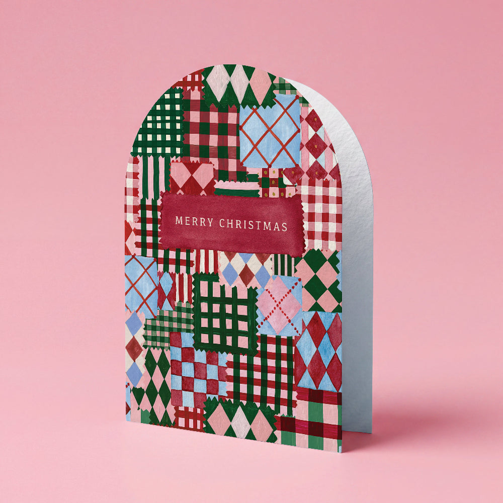 A Christmas greeting card with an arched top and a colorful patchwork pattern of plaid, argyle, and diamond motifs in green, red, pink, and blue. A dark red banner across the center reads 'MERRY CHRISTMAS' in white text.
