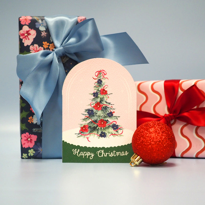Gift card with Christmas tree design, floral-patterned box, and red ornament on a light gray background