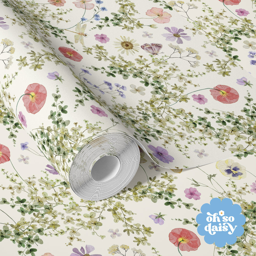 Close-up of Secret Garden wallpaper showing delicate wildflowers, trailing greenery and soft pastel botanical details on a cream background