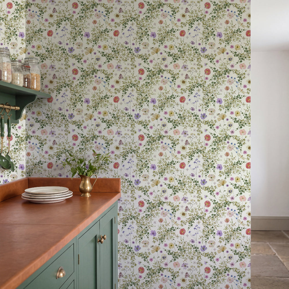 Floral wallpaper with a dense pattern of small green leaves and multicolored flowers on a white background, shown in a kitchen setting behind a green cabinet with a copper countertop.