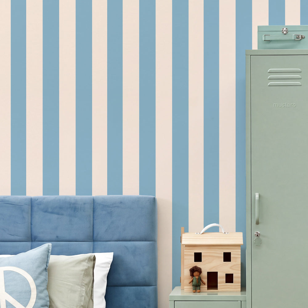 A styled bedroom corner featuring light blue and cream vertical striped wallpaper, a blue tufted headboard, a mint green locker, and a small wooden house toy on a matching side table.