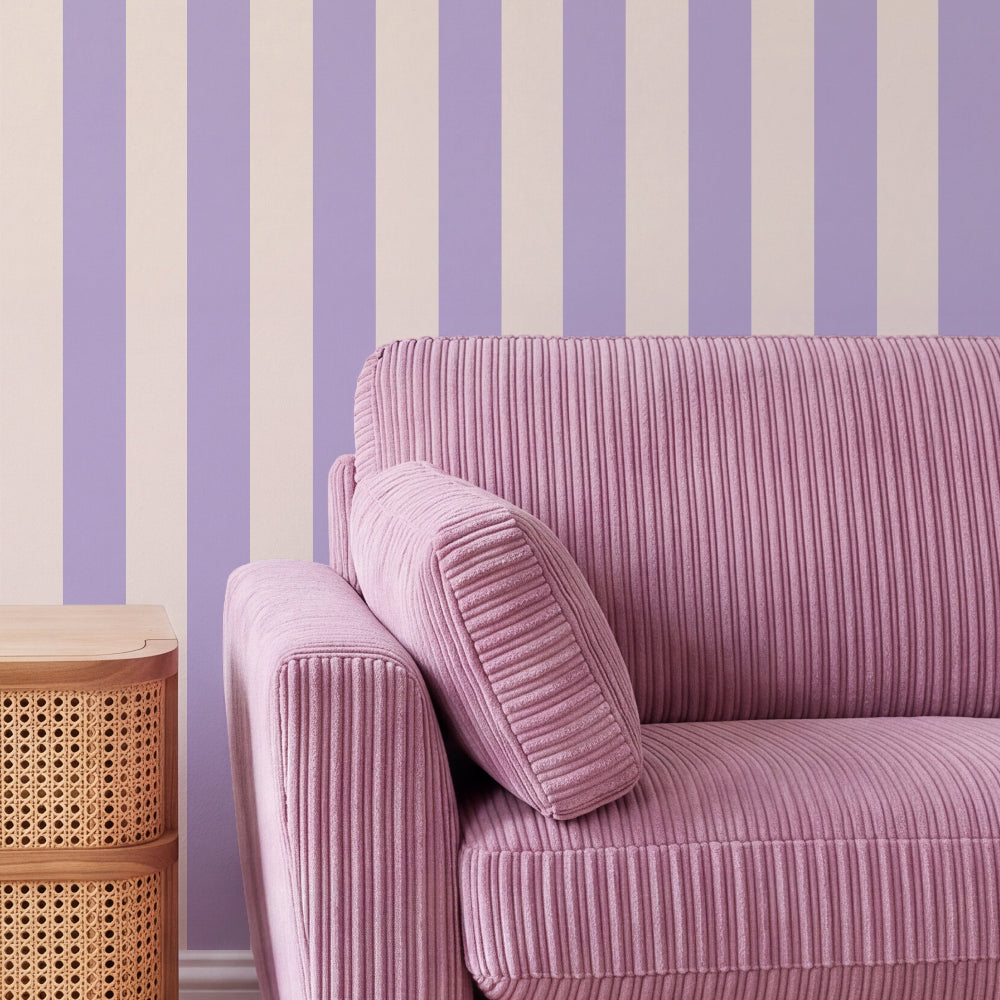 A close-up of a pink ribbed corduroy sofa with a matching cushion, set against a wall with vertical lavender and cream stripes.